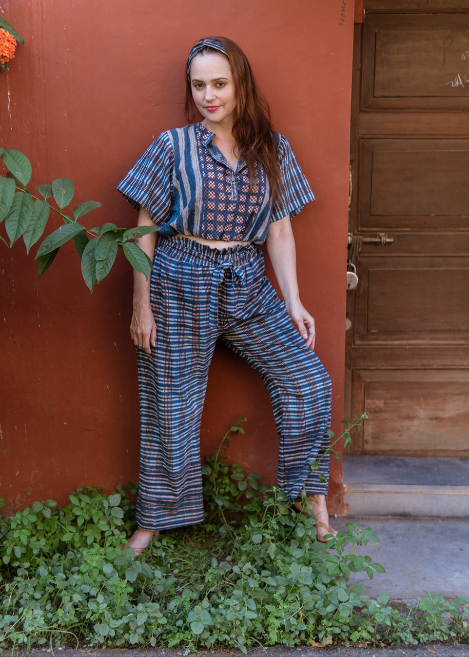 Woman standing against a terracotta wall wearing a hand block printed indigo co-ord set featuring a button-down crop blouse and drawstring pants, exuding a relaxed and confident vibe.