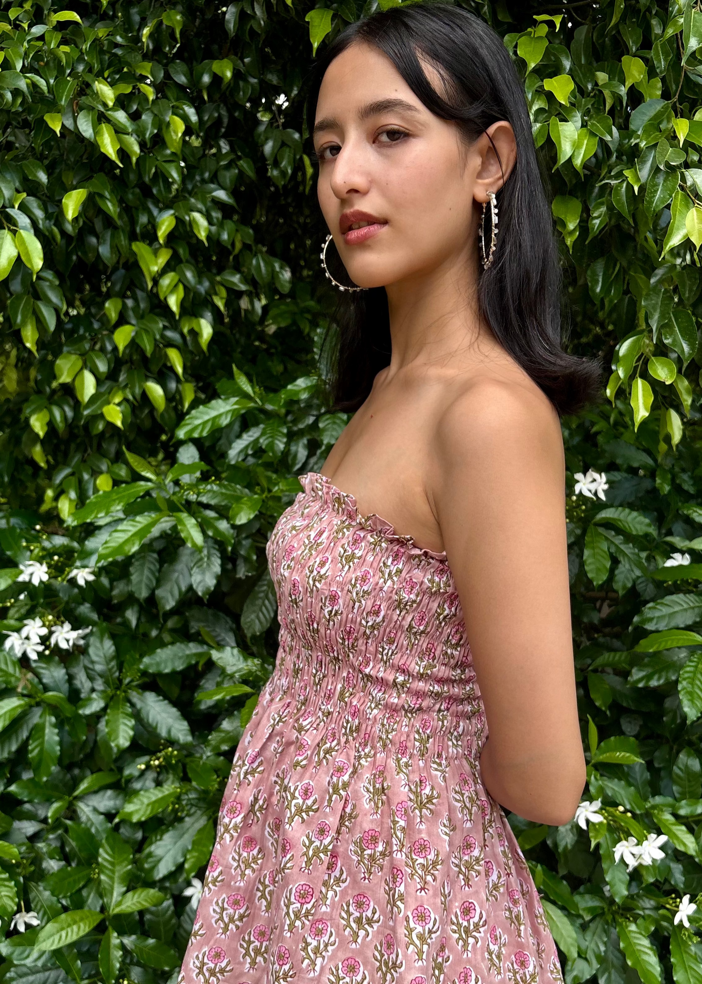 Woman wearing a pink strapless PuffBindi- smocked tops That Romeo dress standing in front of green foliage