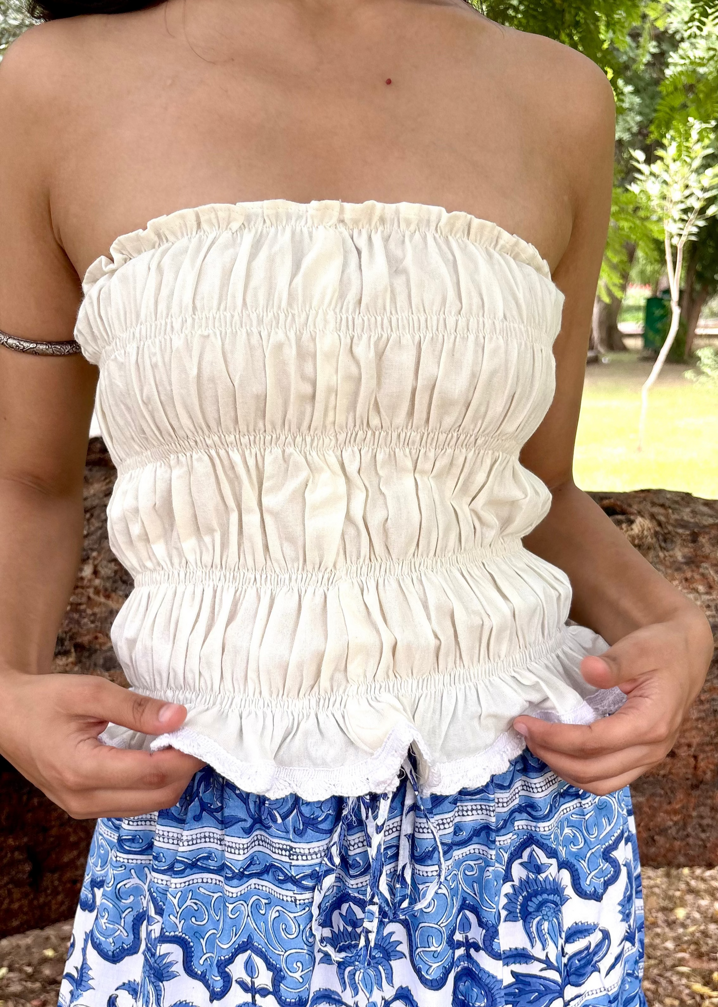 Person wearing a white Ivory Charm Top That Romeo strapless top with ruffles and blue patterned pants outdoors.
