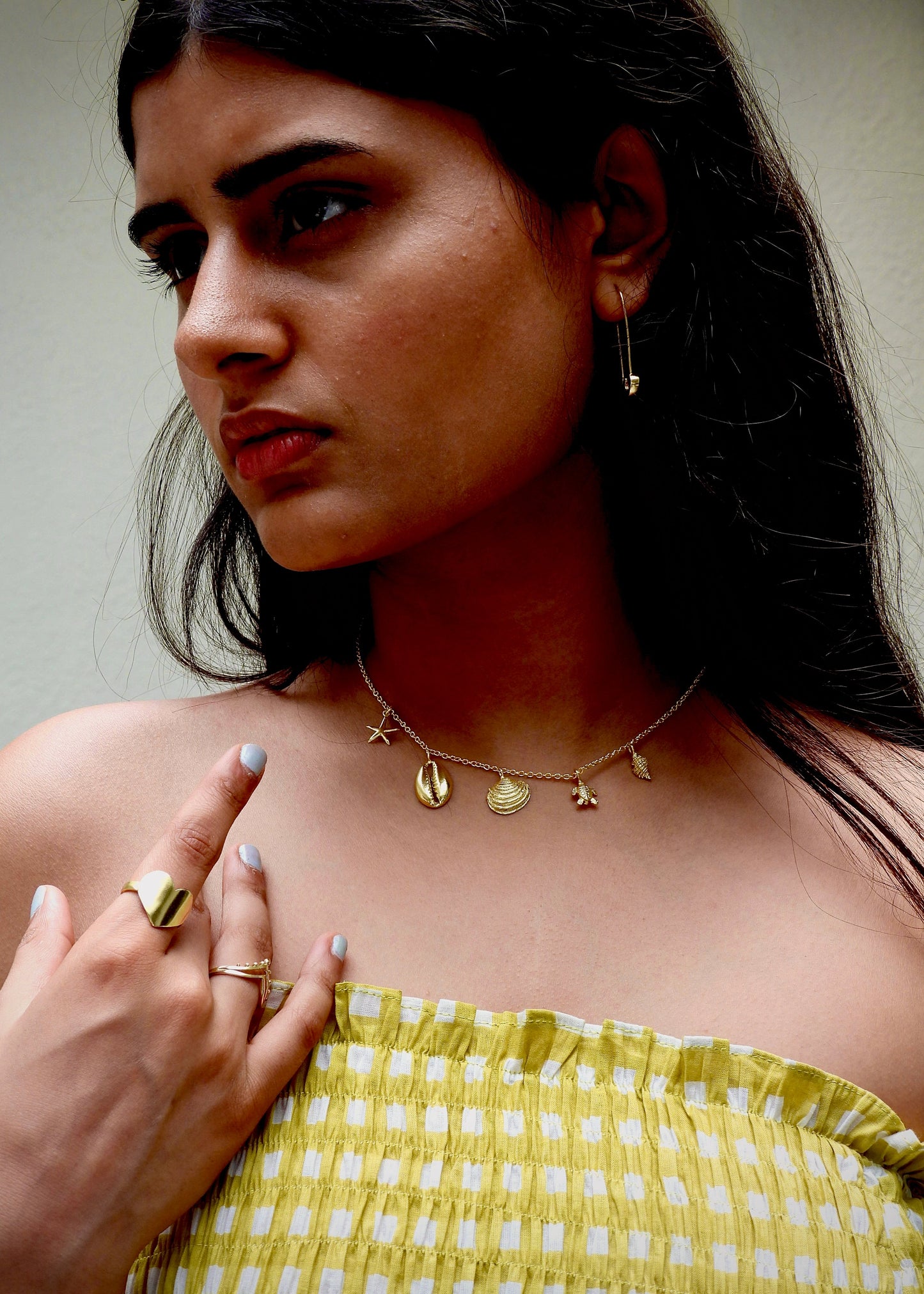 Woman wearing a seashell addict That Romeo gold Plated jewelry including a necklace, earrings, ring, and bangles on a white background