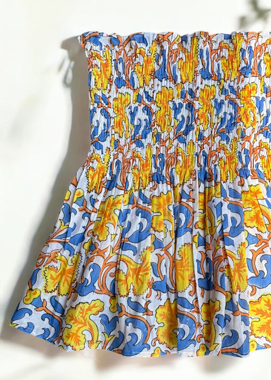 A strapless cotton smocked top with a bold yellow, blue, and orange baroque floral print, flared below the bust and laid flat under soft shadows by That Romeo