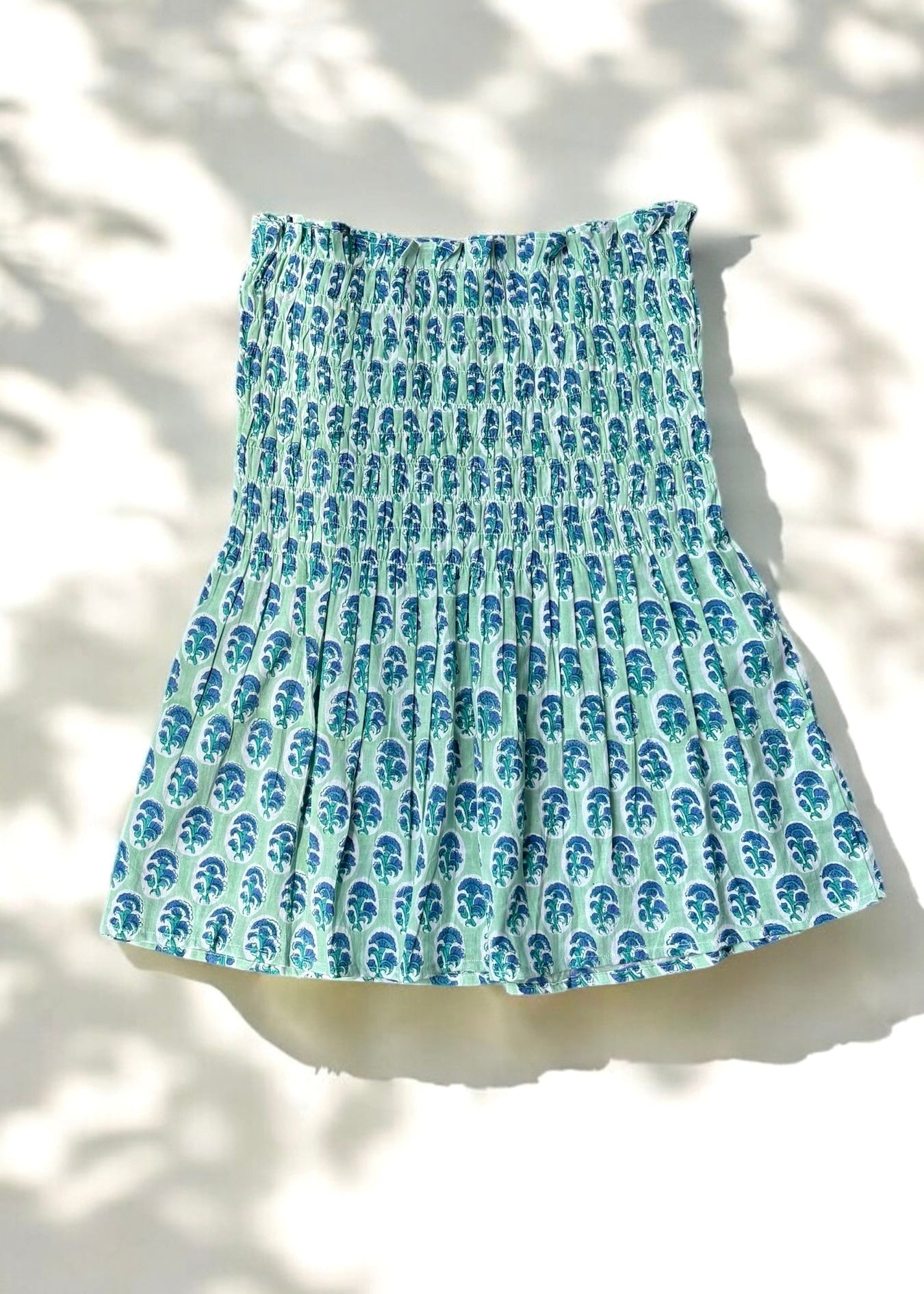 A mint and blue strapless smocked top in cotton with leafy handblock prints, laid flat in soft natural light by That Romeo