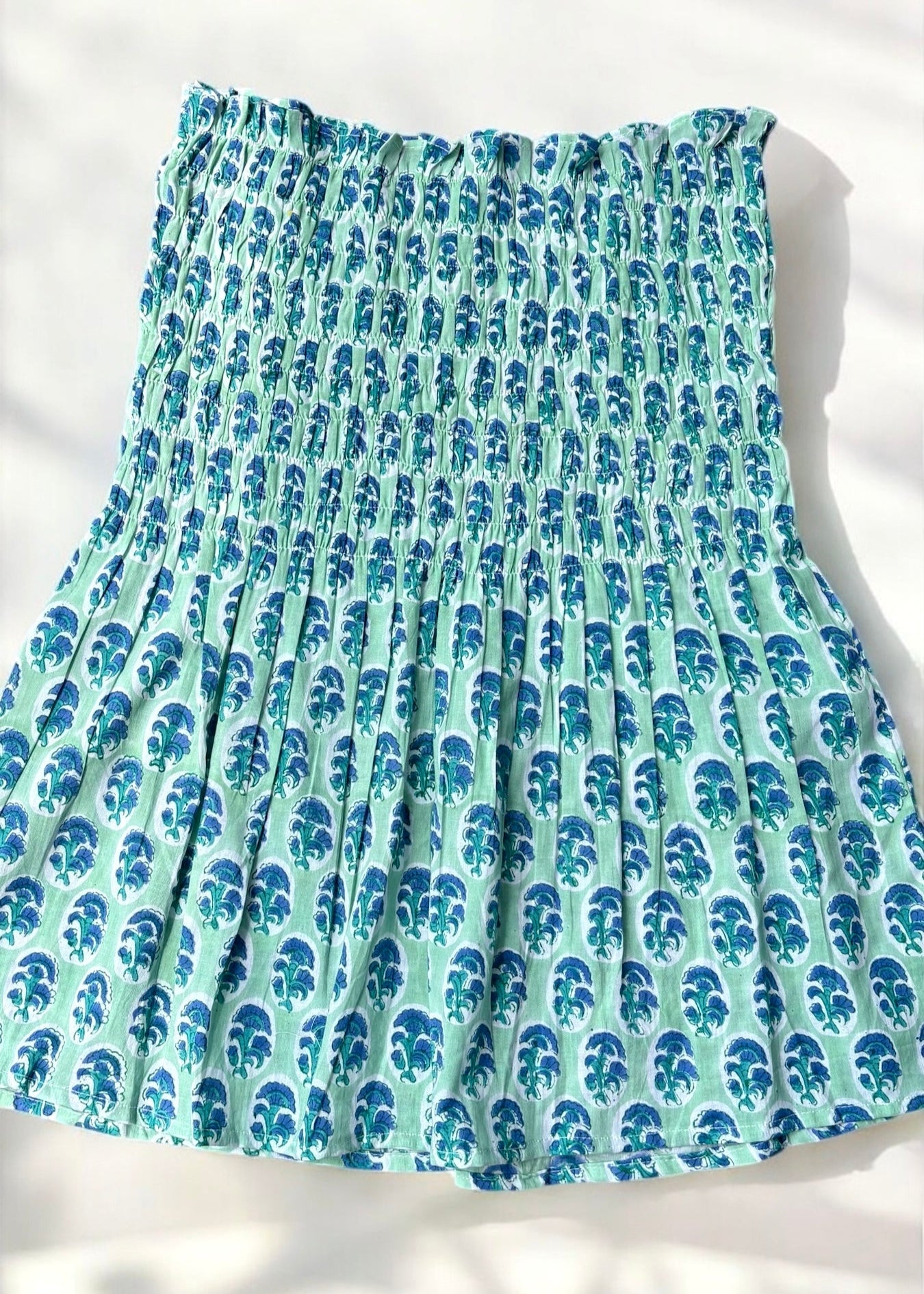 A mint and blue strapless smocked top in cotton with leafy handblock prints, laid flat in soft natural light by That Romeo