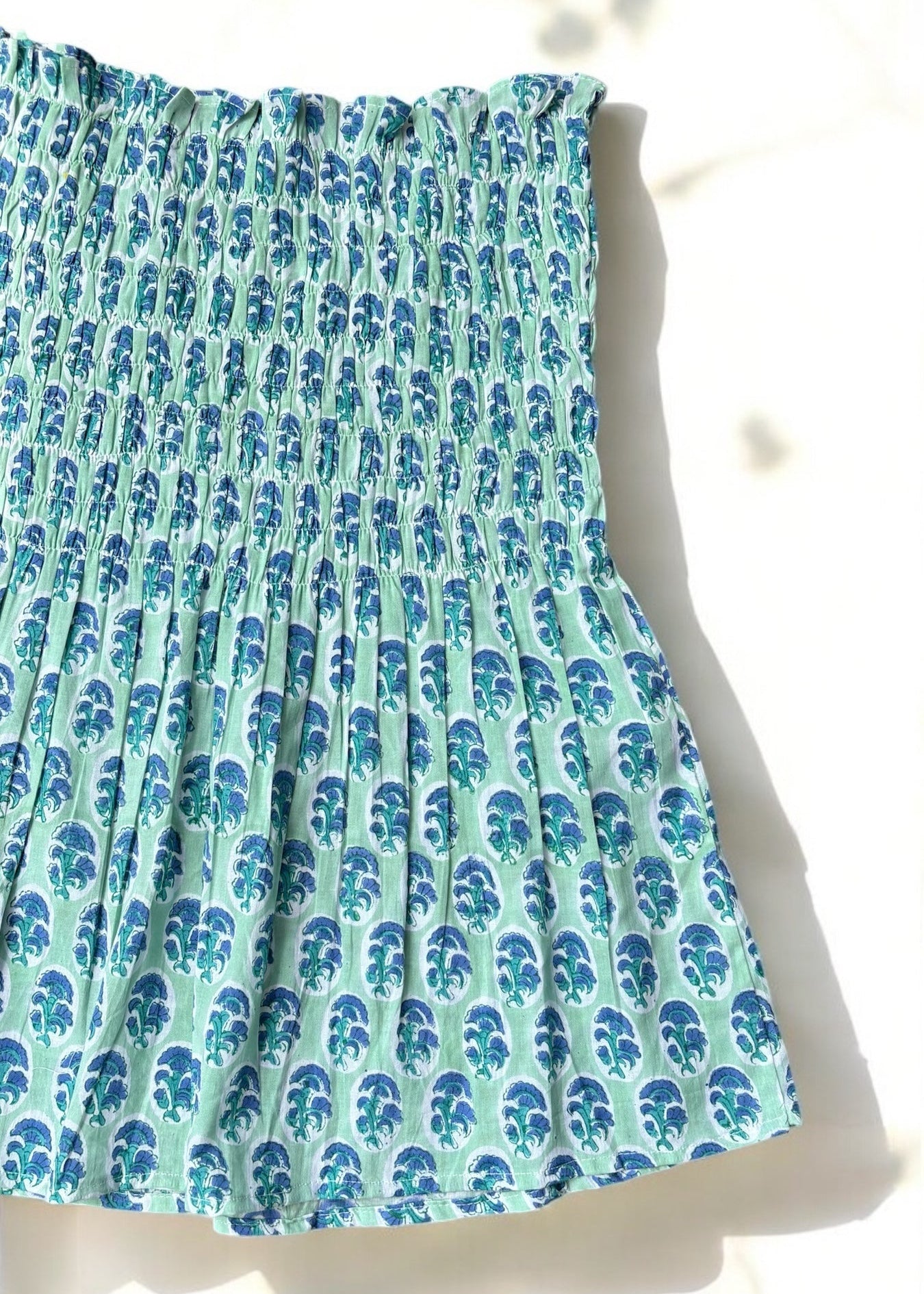 A mint and blue strapless smocked top in cotton with leafy handblock prints, laid flat in soft natural light by That Romeo