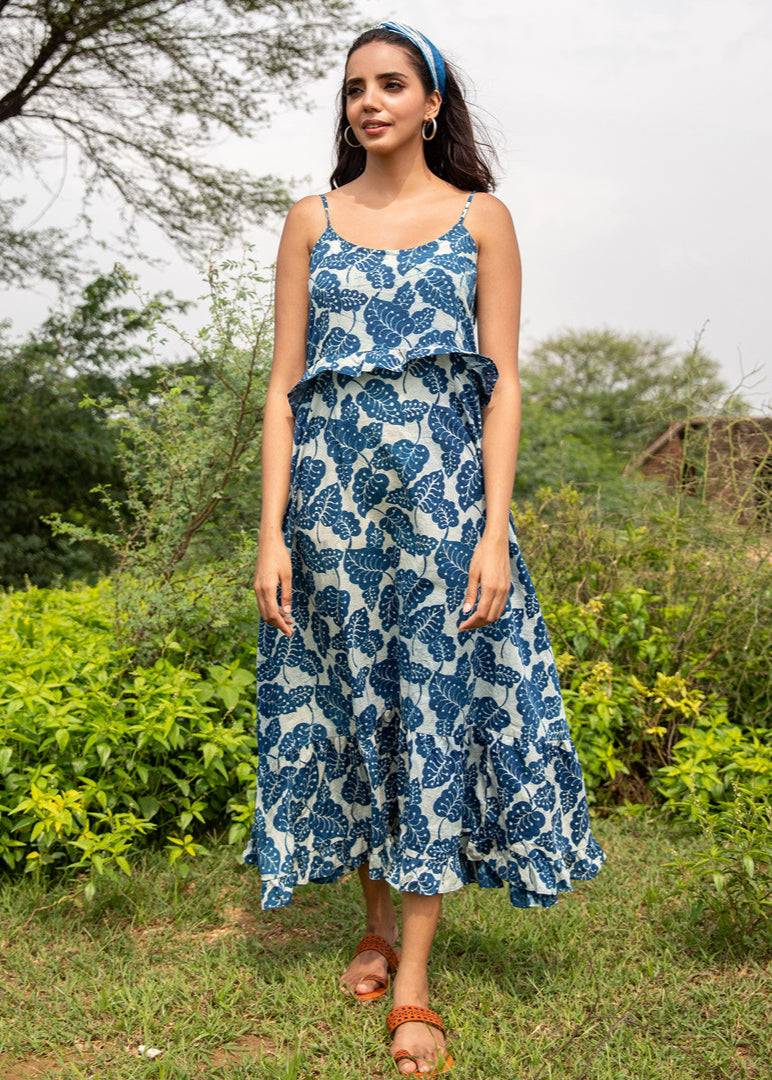 Woman wearing a strappy indigo handblock printed cotton maxi dress with flared silhouette, standing outdoors on a sunny day surrounded by greenery
