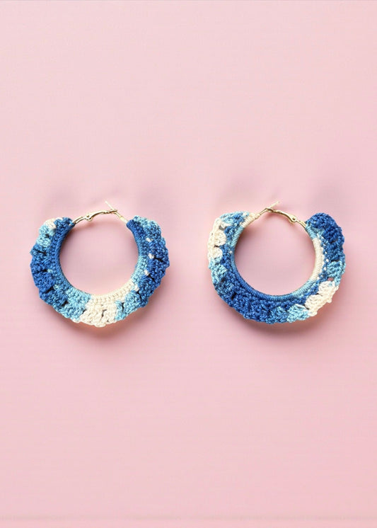 Hand-crocheted blue and ivory hoop earrings by ThatRomeo on a pink background.