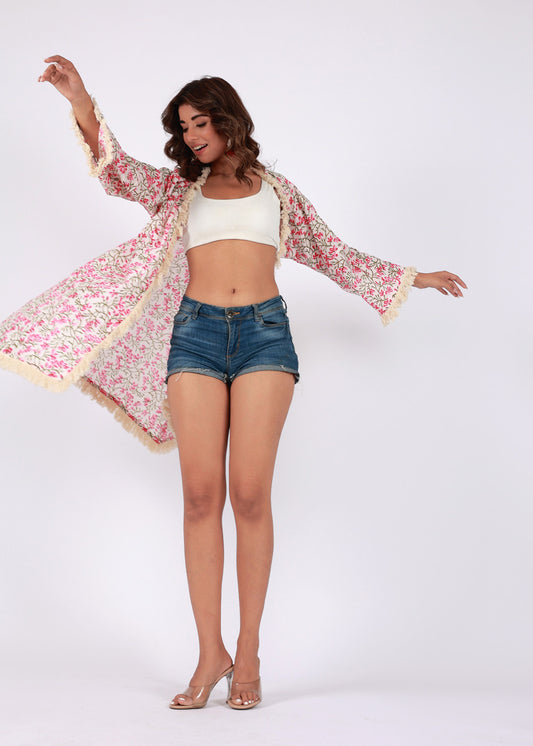 Woman wearing a floral printed cotton shrug with tassel trim, layered over a bralette and shorts, standing with arms spread, smiling confidently.