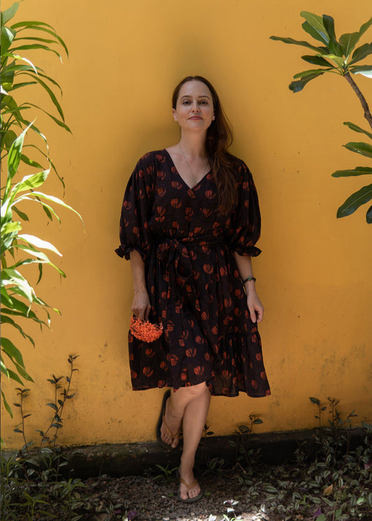 Woman wearing the Night Garden handblock printed boho cotton dress with puffed sleeves, standing against a yellow wall.
