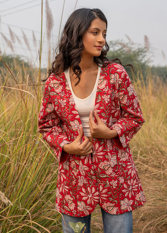 Woman wearing a red hand block printed floral jacket over a white crop top and denim, standing in a grassy field with a serene expression.