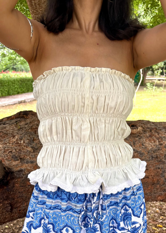 Person wearing a white Ivory Charm Top That Romeo strapless top with ruffles and blue patterned pants outdoors.
