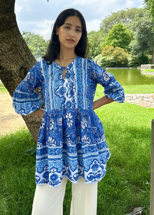Woman wearing a blue and white patterned Floral Whispers Tunic top That Romeo dress standing outdoors near a tree and body of water.