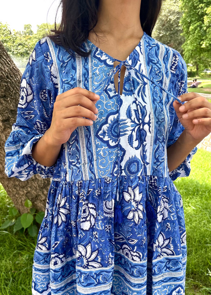 Woman wearing a blue and white patterned Floral Whispers Tunic top That Romeo dress standing outdoors near a tree and body of water.