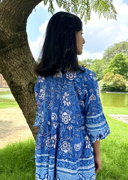 Woman wearing a blue and white patterned Floral Whispers Tunic top That Romeo dress standing outdoors near a tree and body of water.