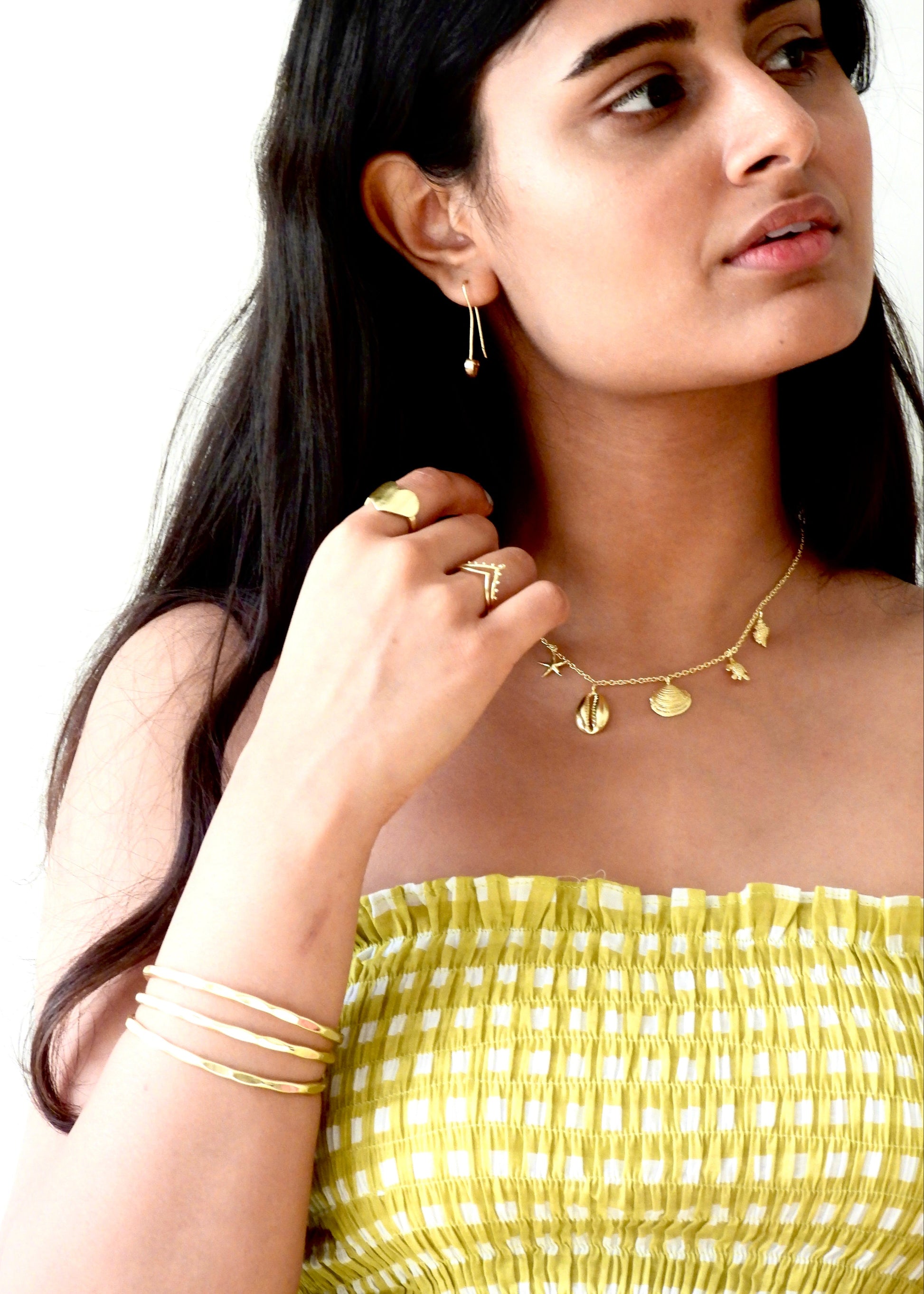 Woman wearing a seashell addict That Romeo gold Plated jewelry including a necklace, earrings, ring, and bangles on a white background