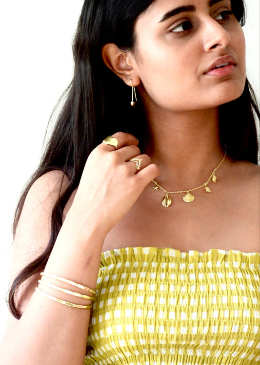 Woman wearing a seashell addict That Romeo gold Plated jewelry including a necklace, earrings, ring, and bangles on a white background