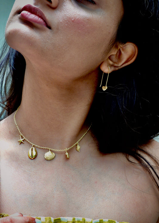 Woman wearing a seashell addict That Romeo gold Plated necklace with shell-shaped pendants.
