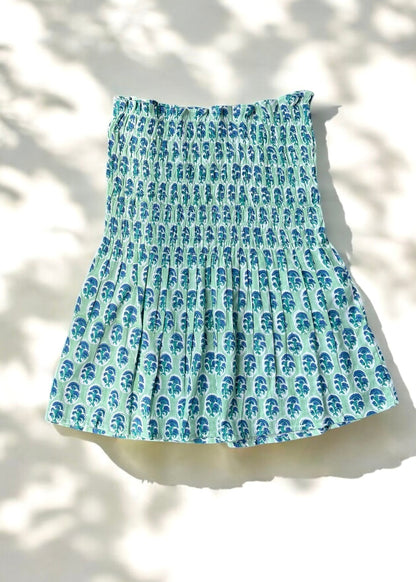 A mint and blue strapless smocked top in cotton with leafy handblock prints, laid flat in soft natural light by That Romeo