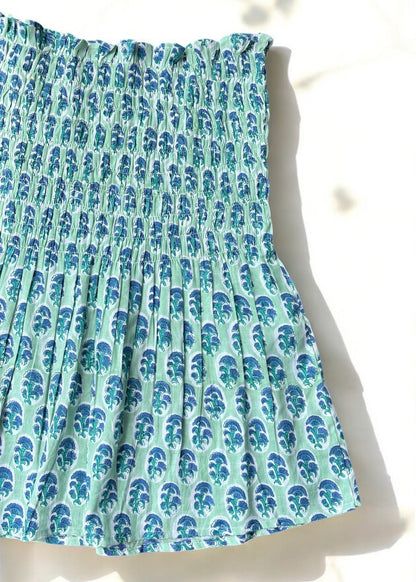 A mint and blue strapless smocked top in cotton with leafy handblock prints, laid flat in soft natural light by That Romeo