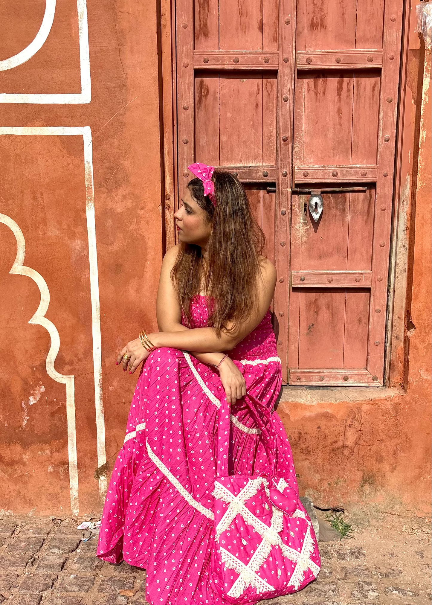 Woman in a pink dress standing in front of a red door with decorative patterns with Pink Bandhani quilted tote bag by That Romeo