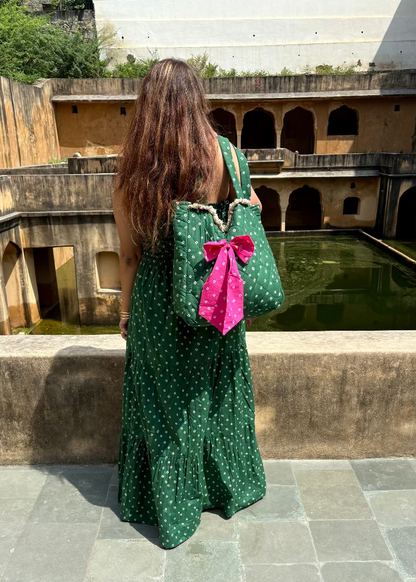 Woman in a green dress with a polka dot pattern and Green Bandhani quilted tote bag with pink bow by That Romeo standing in front of a stone building.