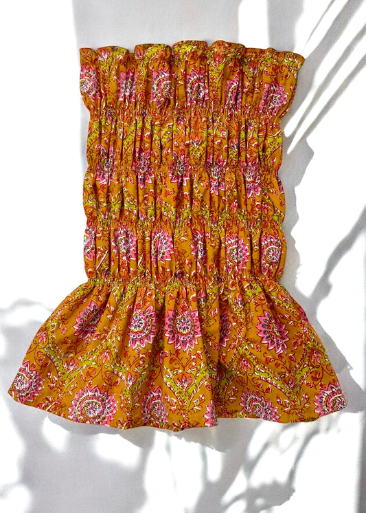 Flat lay of marigold yellow cotton smocked bust top with pink floral print and peplum hem, captured in natural light and shadows.
