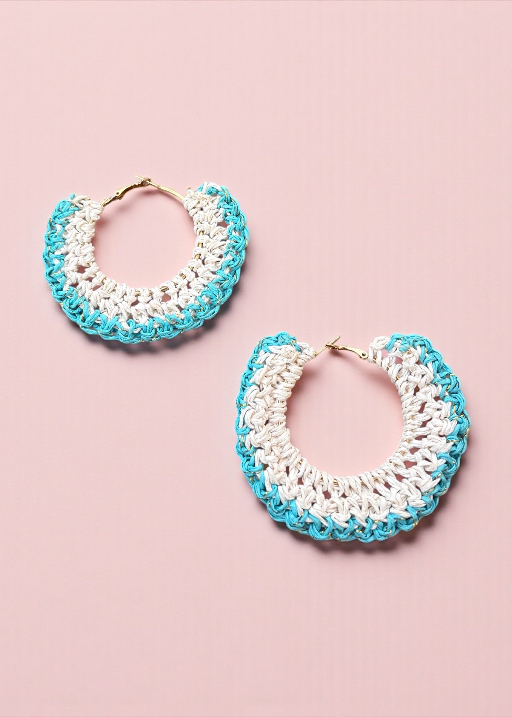 Aqua blue and white crochet hoop earrings by ThatRomeo on a soft pink background.