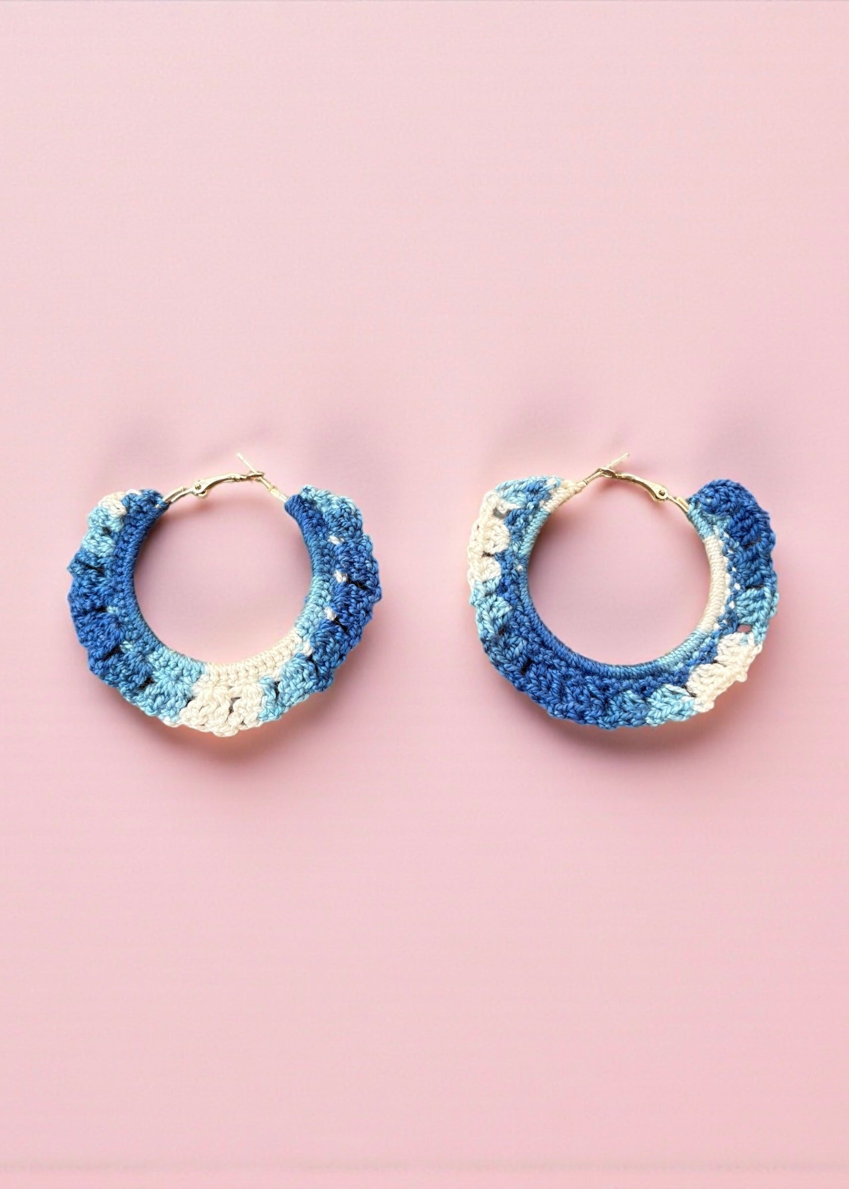 Hand-crocheted blue and ivory hoop earrings by ThatRomeo on a pink background.