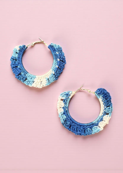 Hand-crocheted blue and ivory hoop earrings by ThatRomeo on a pink background.