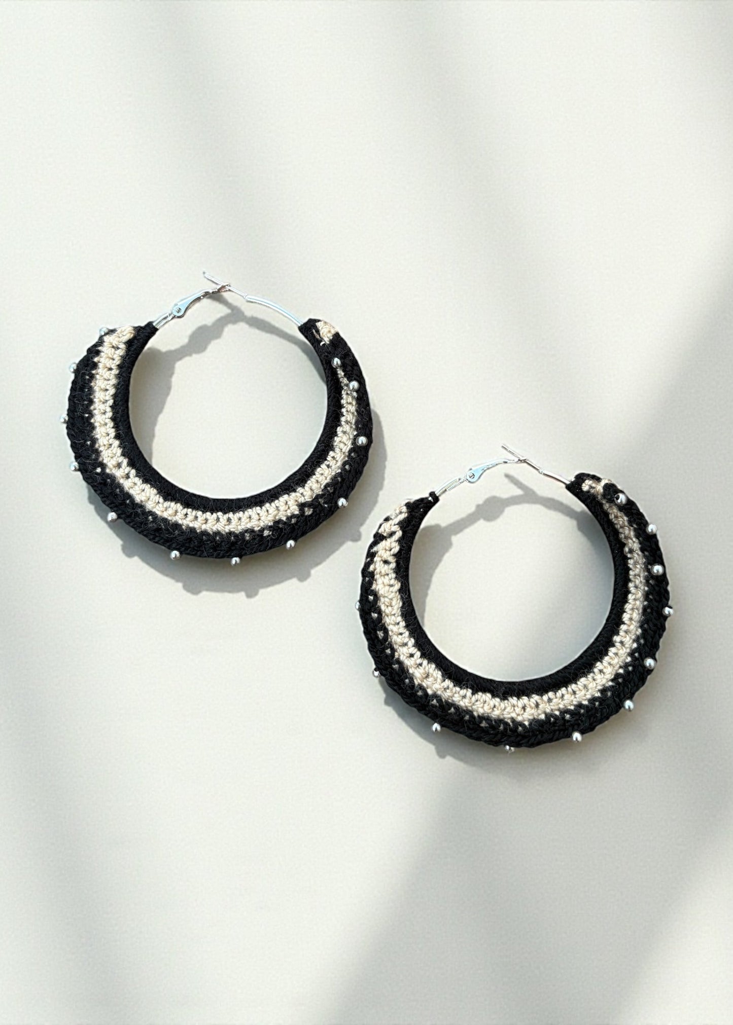 Black and cream crochet hoop earrings with bead accents by ThatRomeo on a soft-light background.