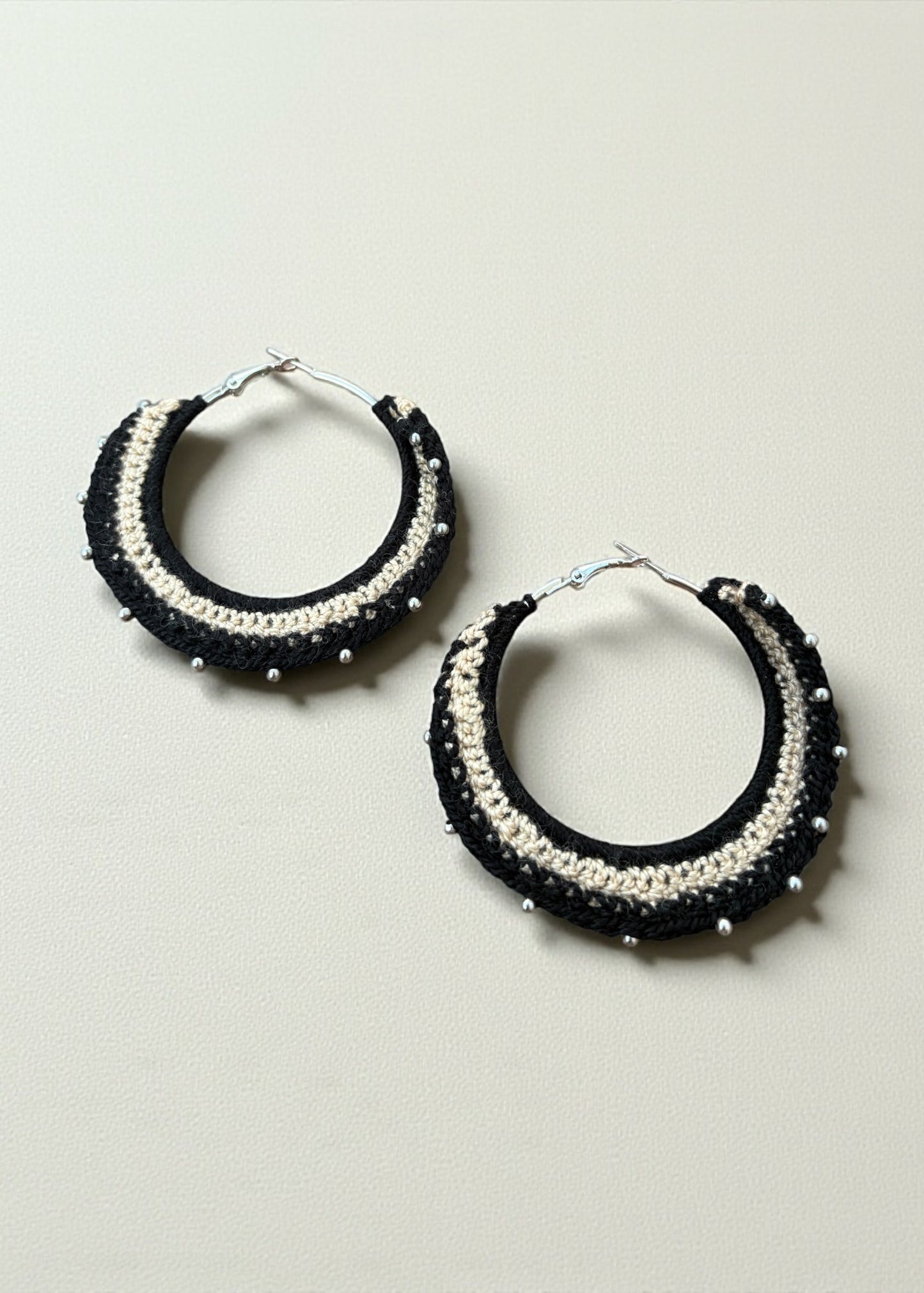 Black and cream crochet hoop earrings with bead accents by ThatRomeo on a soft-light background.