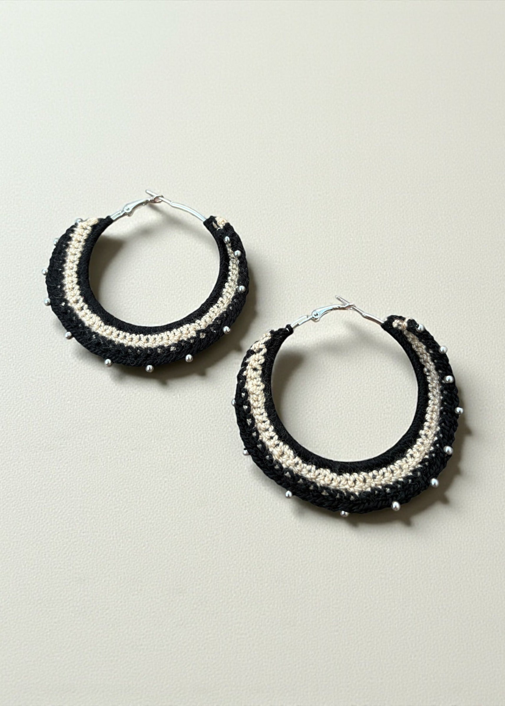 Black and cream crochet hoop earrings with bead accents by ThatRomeo on a soft-light background.