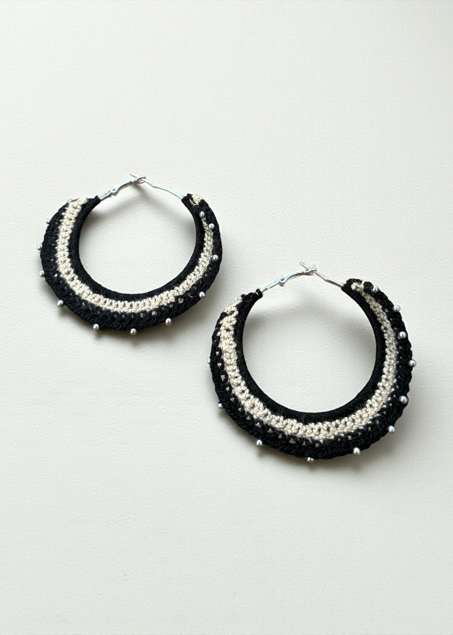 Black and cream crochet hoop earrings with bead accents by ThatRomeo on a soft-light background.