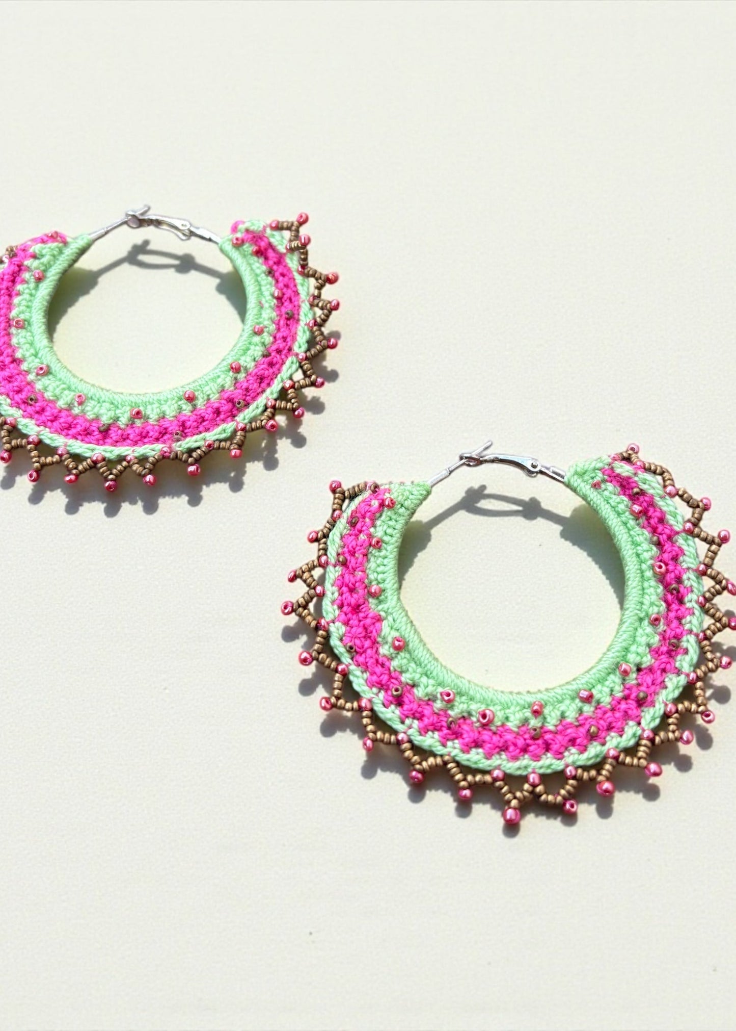 Neon green and hot pink crochet hoop earrings with gold and pink beads by ThatRomeo on a light background.
