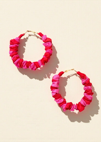 Pink and red ruched fabric hoop earrings by ThatRomeo on a colour-blocked background.