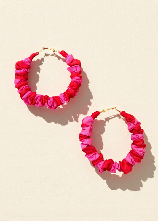 Pink and red ruched fabric hoop earrings by ThatRomeo on a colour-blocked background.