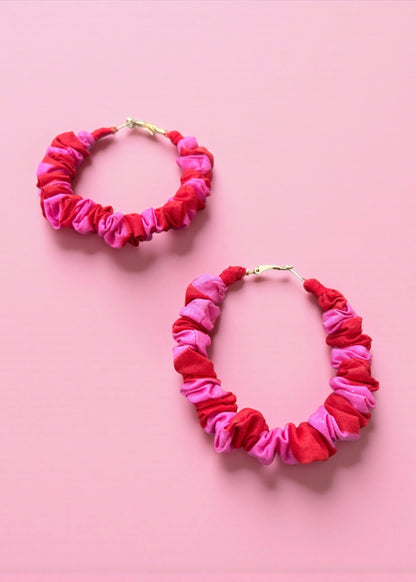 Pink and red ruched fabric hoop earrings by ThatRomeo on a colour-blocked background.