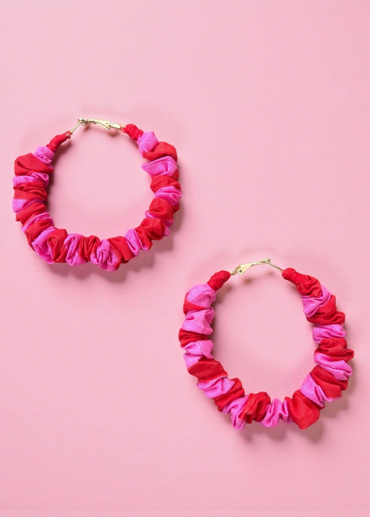 Pink and red ruched fabric hoop earrings by ThatRomeo on a colour-blocked background.