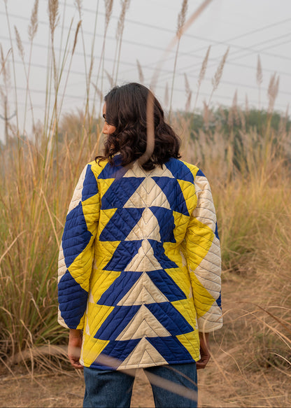 Model wearing ThatRomeo’s Sky Circuit Quilted Jacket — cotton patchwork jacket in cobalt blue, yellow, and cream tones with open front.