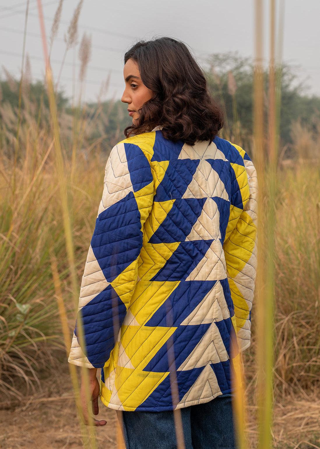 Model wearing ThatRomeo’s Sky Circuit Quilted Jacket — cotton patchwork jacket in cobalt blue, yellow, and cream tones with open front.